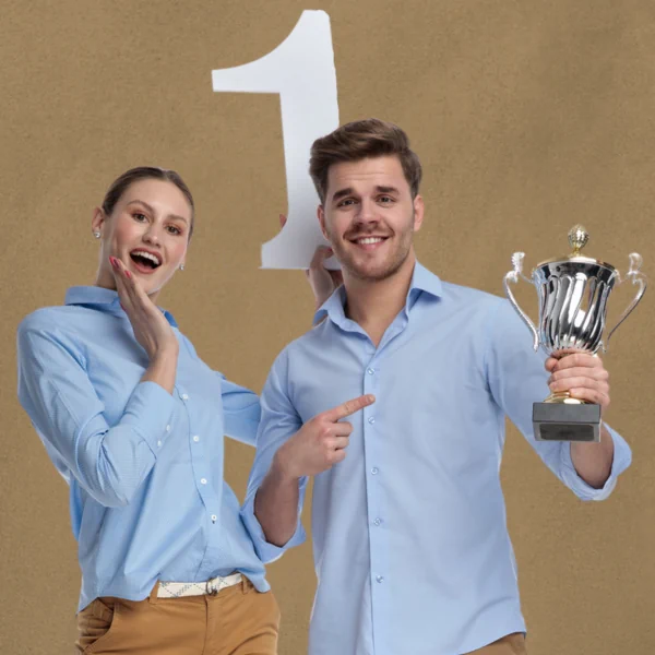 Ein Mann hebt einen Pokal nach vorne, während eine Frau ein Schild mit der Nummer 1 hochhebt.